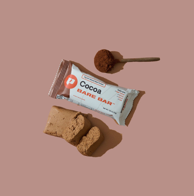 Cocoa Bare Bar with a spoonful of cocoa powder on a beige background